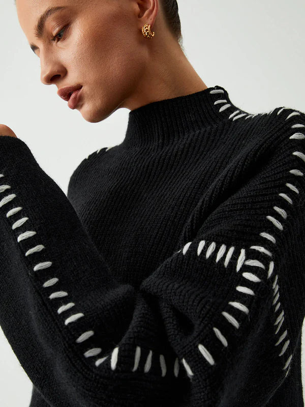 Black sweater with white zigzag patterns on sleeves and neckline against a neutral background