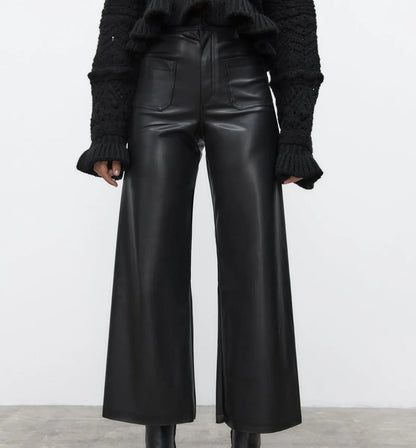 Person wearing black leather wide-leg pants with a plain background