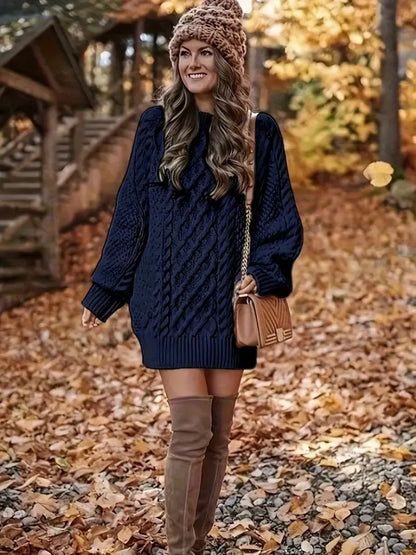 Woman in a navy blue cable knit sweater and brown over-the-knee boots standing in an autumn setting.