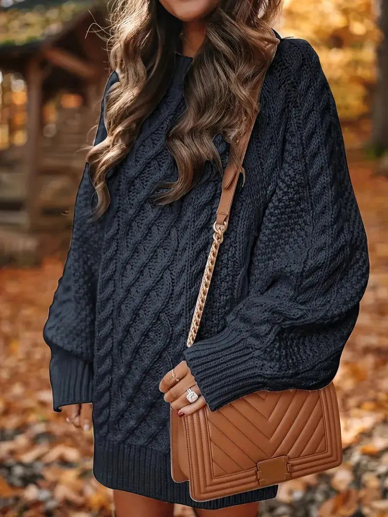 Person wearing a dark blue cable knit sweater with a brown leather handbag in an autumn setting.