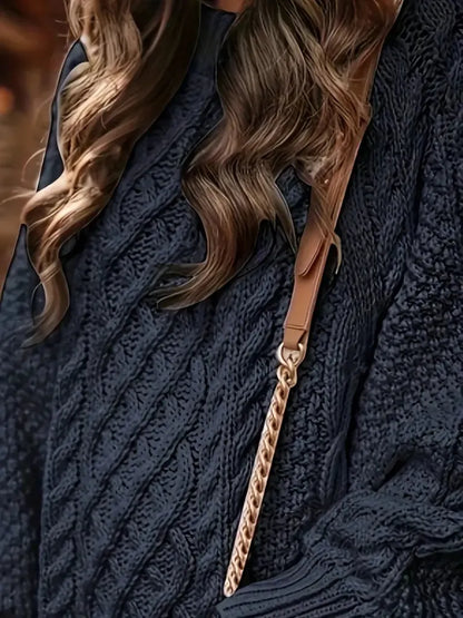 Close-up of a person wearing a dark blue knitted sweater with a gold chain strap over their shoulder.