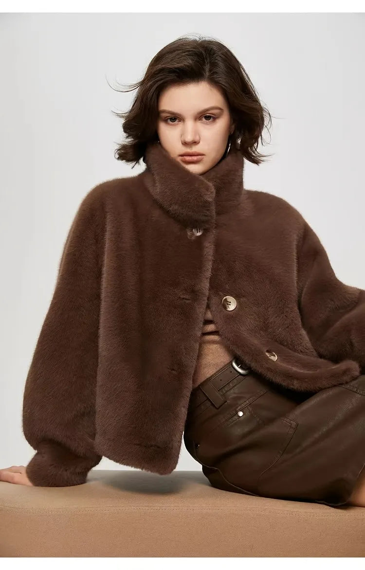 Person wearing a brown fur coat sitting on a beige surface with a plain background