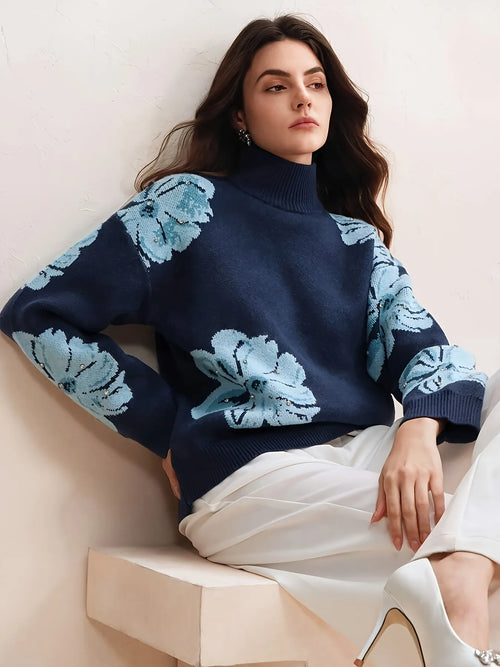 Woman wearing a navy sweater with light blue floral patterns sitting on a beige chair.