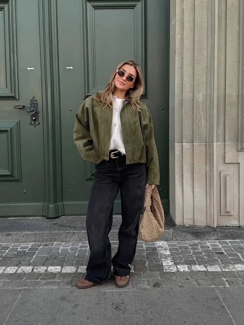 Woman in green jacket and black pants standing in front of a green door.