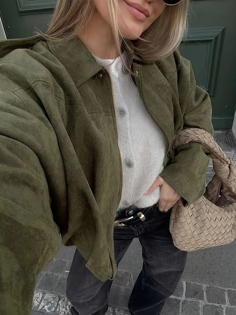 Person wearing a green jacket and white sweater, holding a woven beige bag.