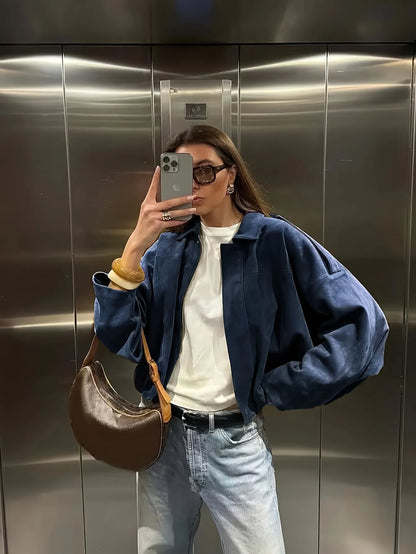 Person taking a mirror selfie wearing a blue jacket, white shirt, and jeans in an elevator.