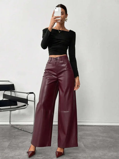 Person wearing maroon leather wide-leg pants with a black top and shoes in a minimalistic setting.