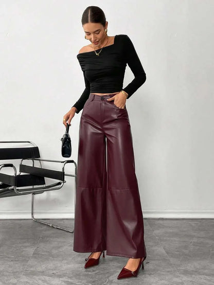 Woman wearing a black top and maroon wide-leg pants standing against a white wall.