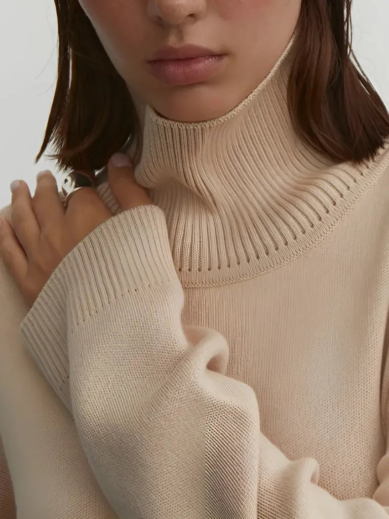 Close-up of a person wearing a beige turtleneck sweater against a neutral background