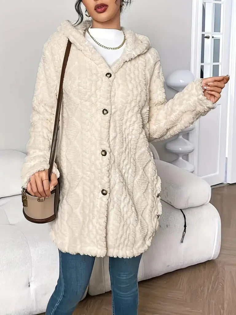 Person wearing a cream-colored sherpa coat in a room with white furniture.