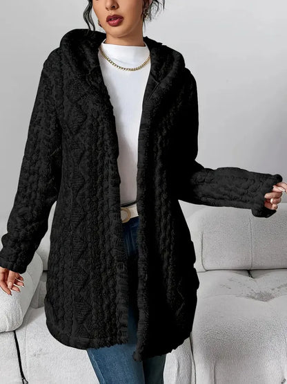 Person wearing a black cable knit cardigan in a neutral setting