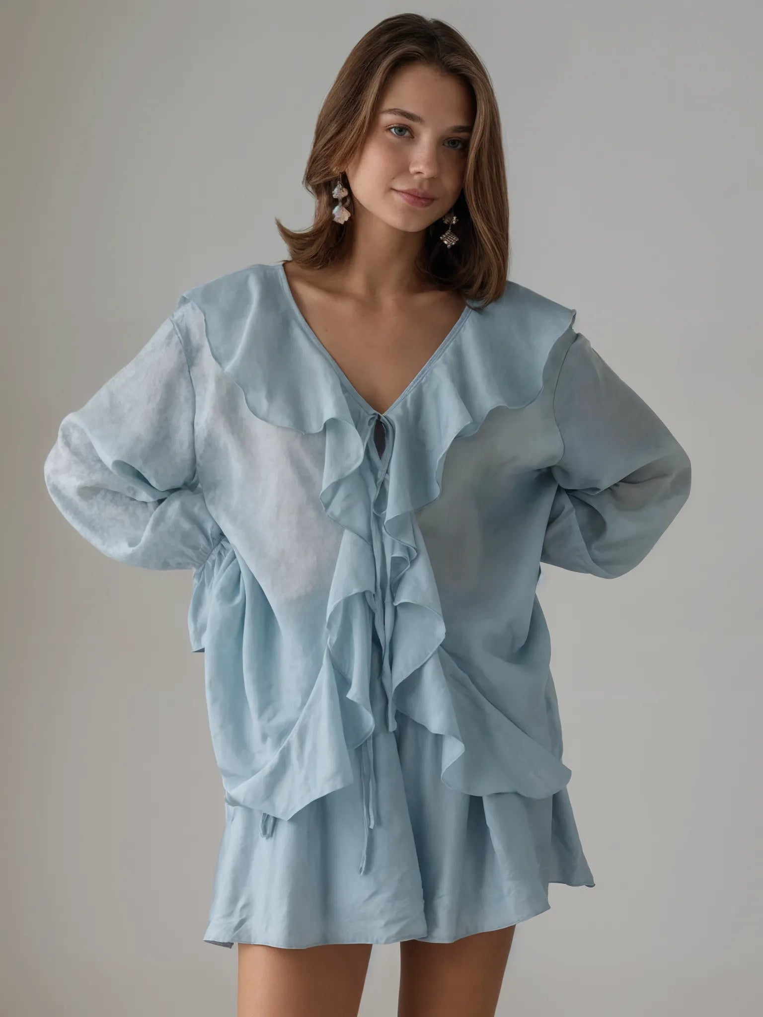 Woman wearing a light blue dress with ruffled layers against a plain background