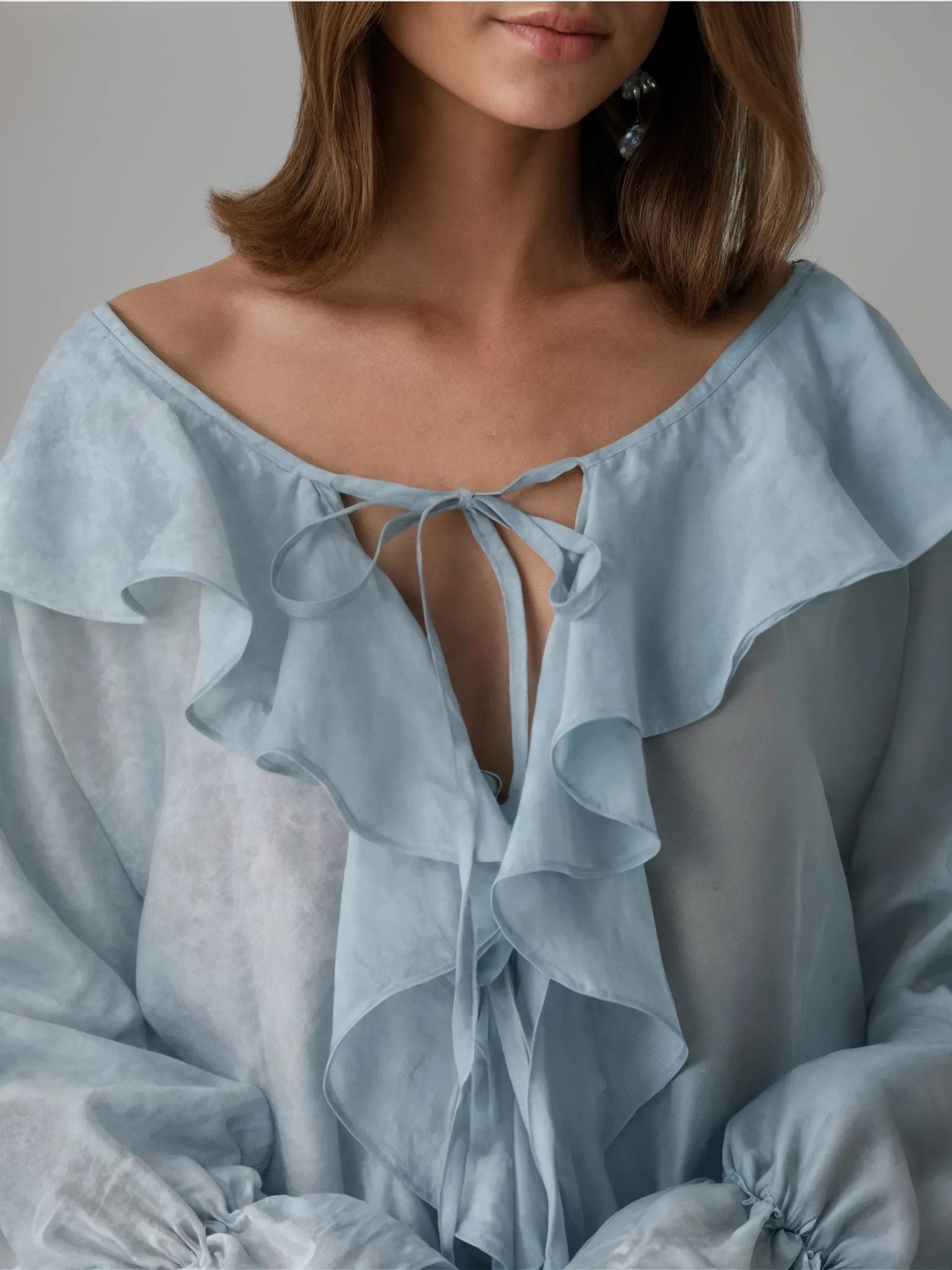 Light blue blouse with ruffled details and a tie front, worn by a person.