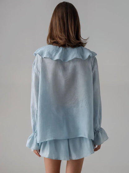 Light blue blouse with ruffled collar and cuffs worn by a person on a plain background