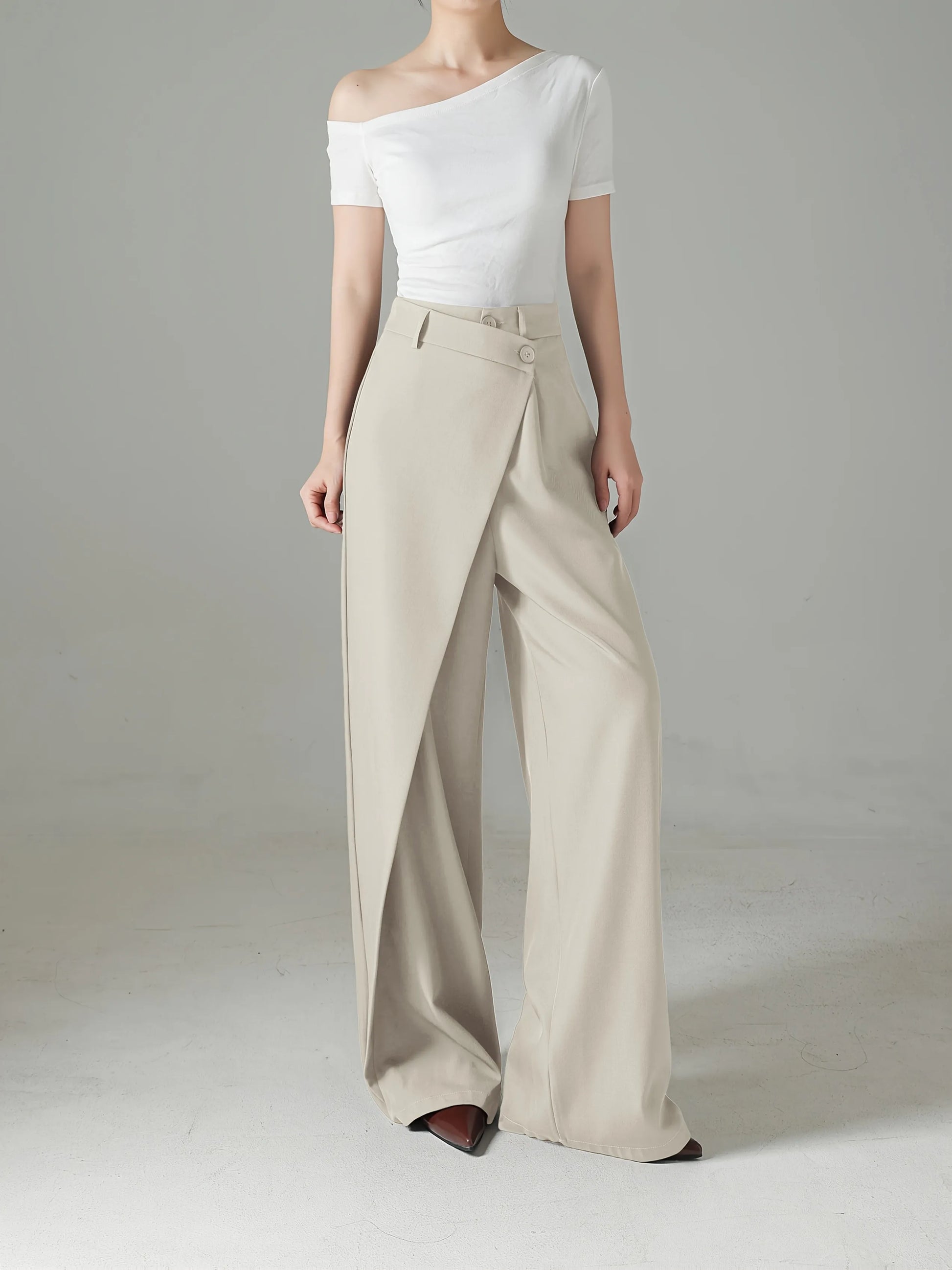 Person wearing a white off-shoulder top and beige wide-leg pants on a plain background