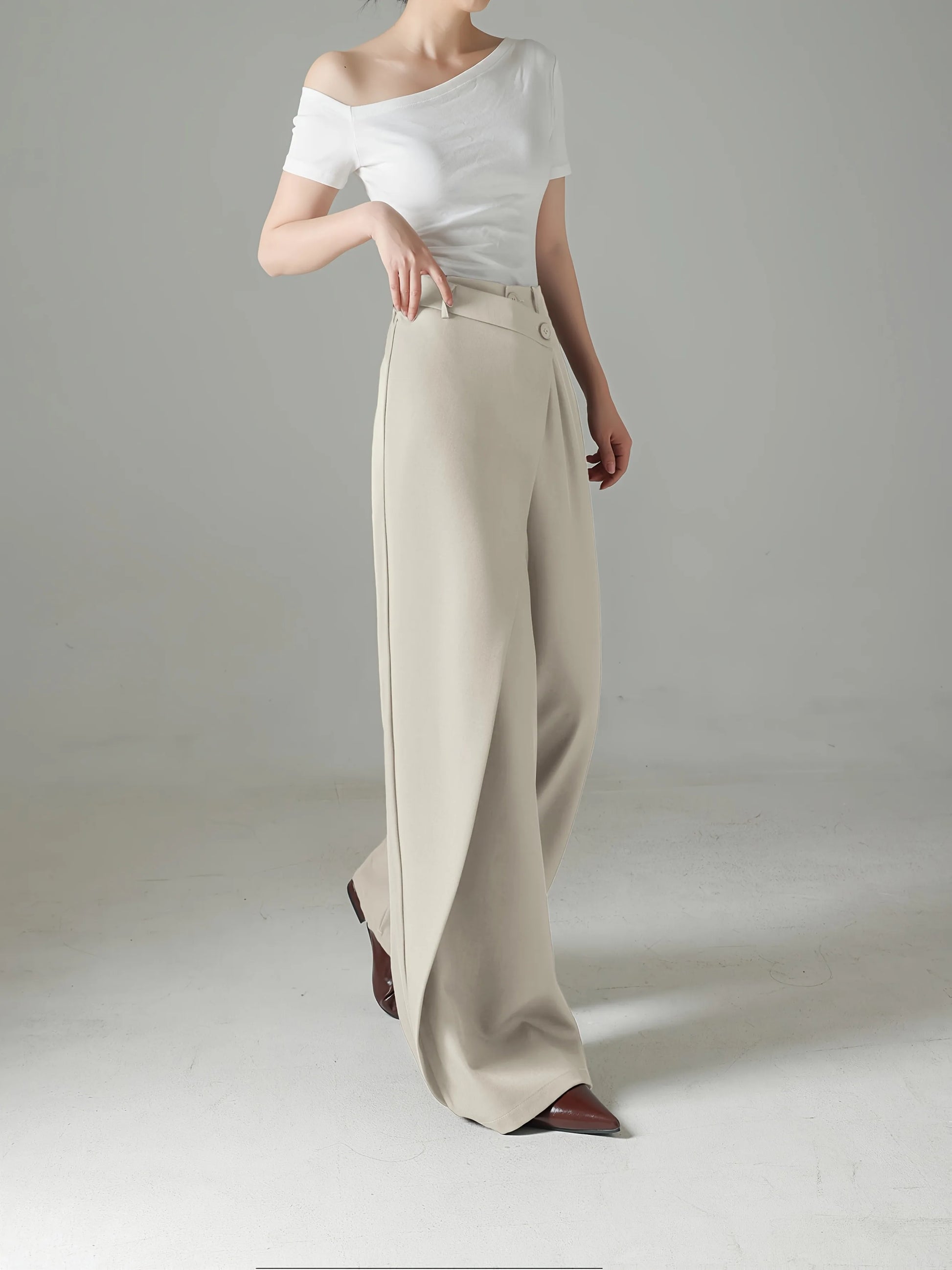 Person wearing a white off-shoulder top and beige wide-leg pants on a plain background