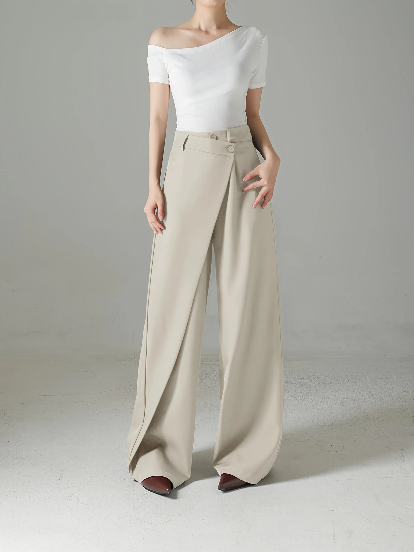 Person wearing a white off-shoulder top and beige wide-leg pants on a plain background