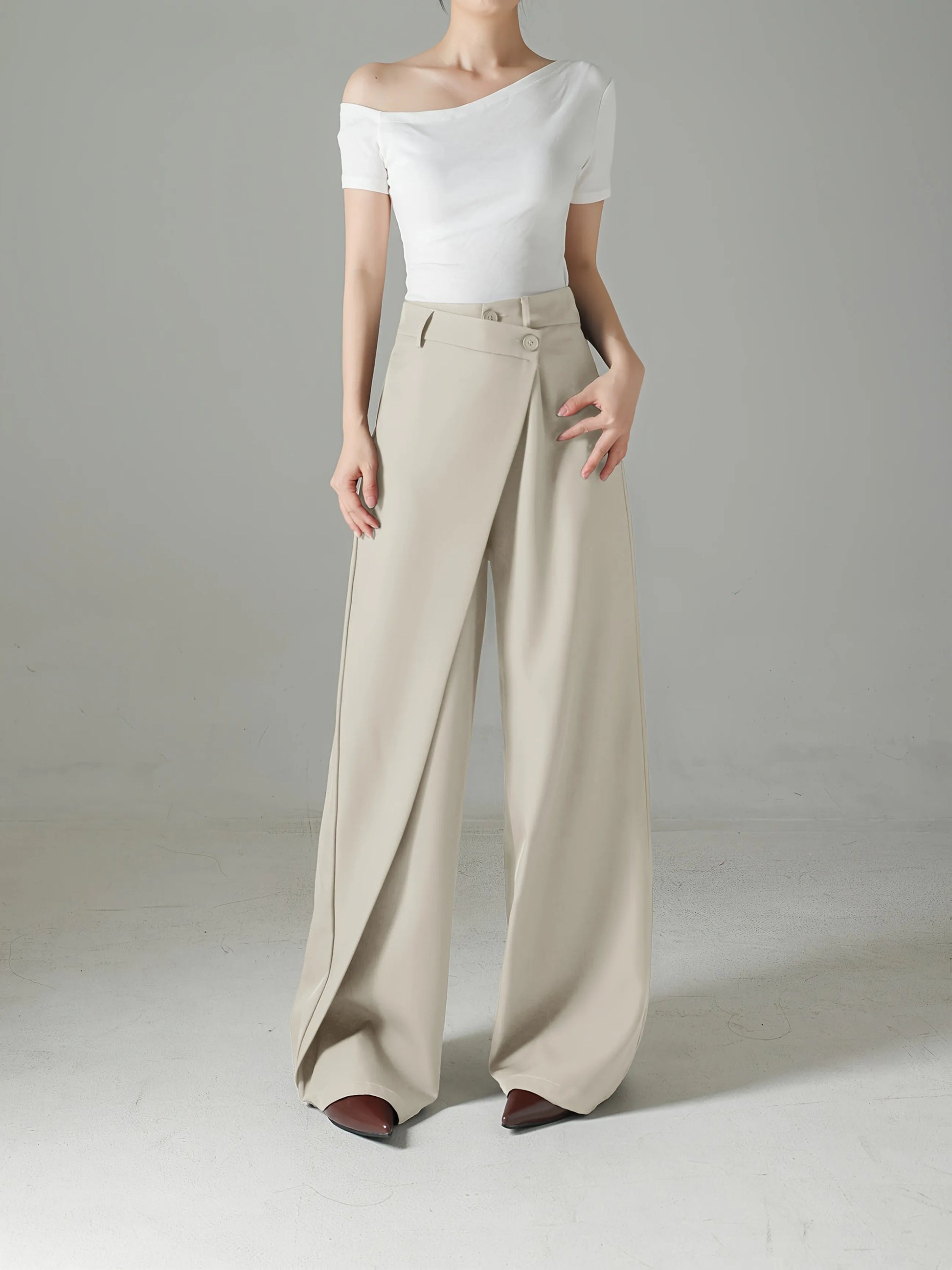Person wearing a white off-shoulder top and beige wide-leg pants on a plain background