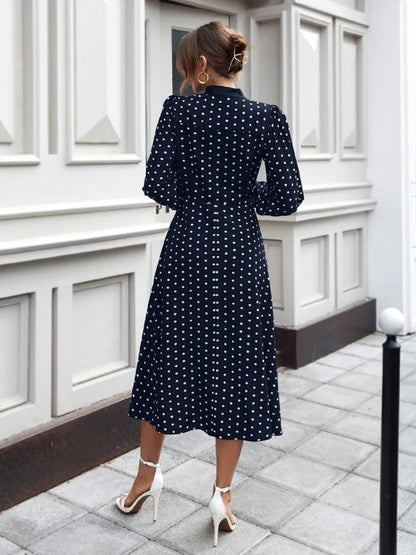 Woman wearing a navy blue dress with white polka dots in an urban setting.