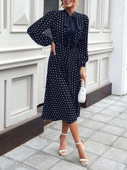 Woman wearing a navy blue dress with white polka dots, standing on a sidewalk.
