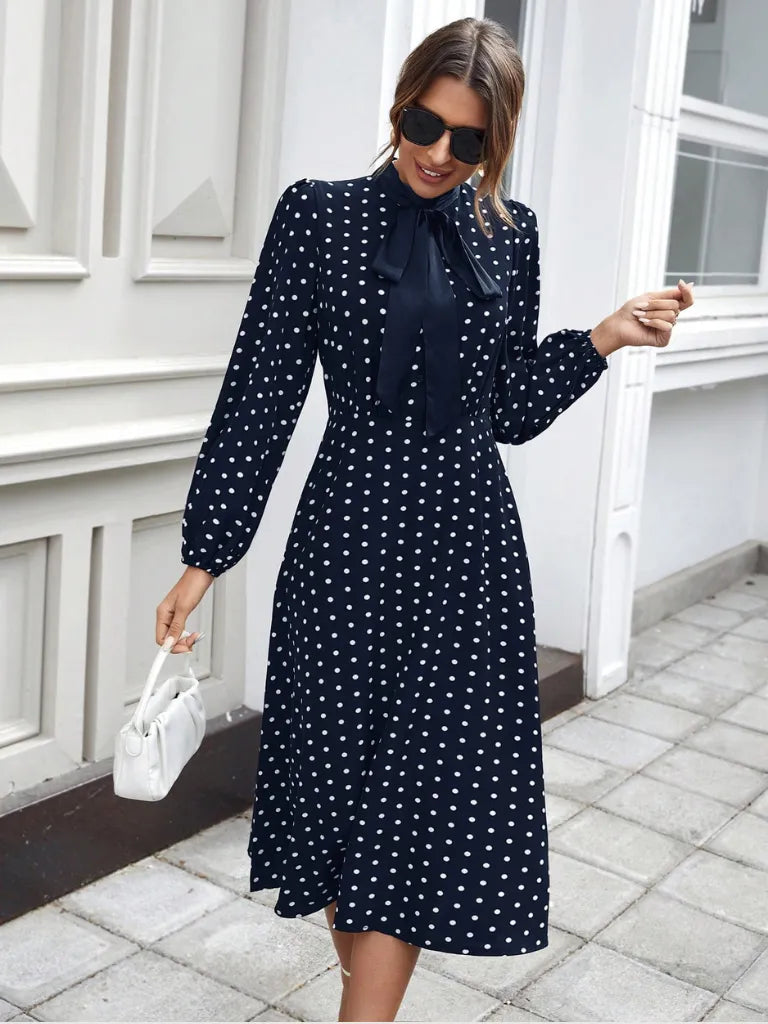 Woman wearing a navy polka dot dress standing outside a building.