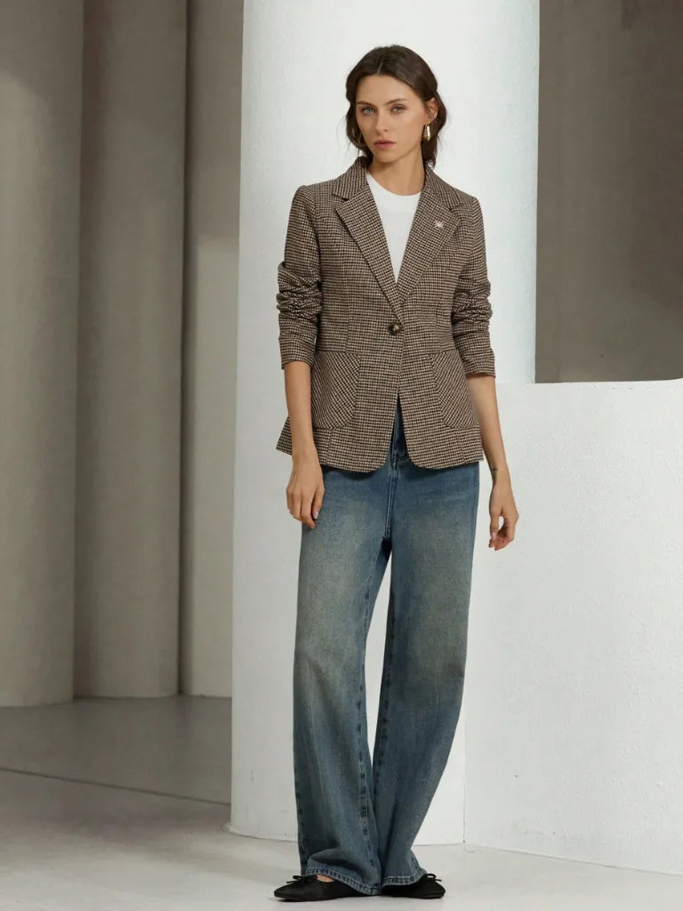 Woman wearing a brown blazer and blue jeans in a minimalistic setting