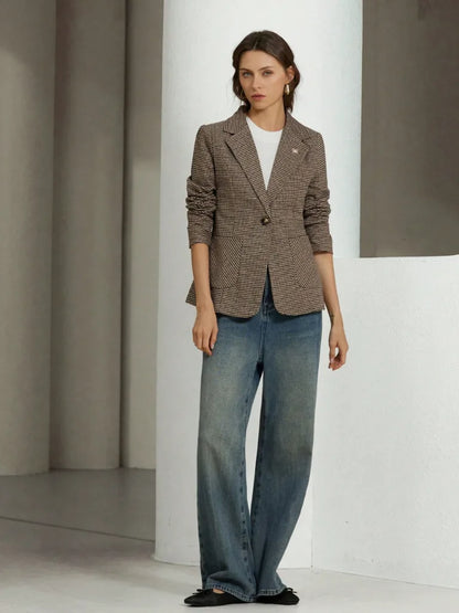 Woman wearing a brown blazer and blue jeans in a minimalistic setting