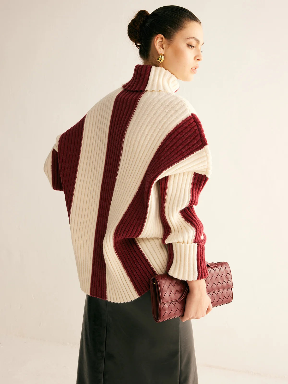 Woman wearing a striped sweater holding a clutch against a plain background