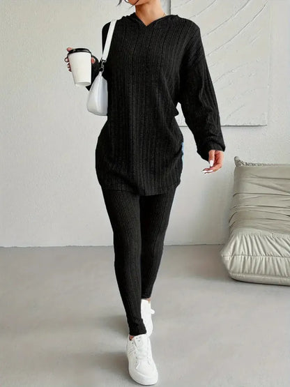 Person wearing a black outfit with white sneakers in a minimalistic room.