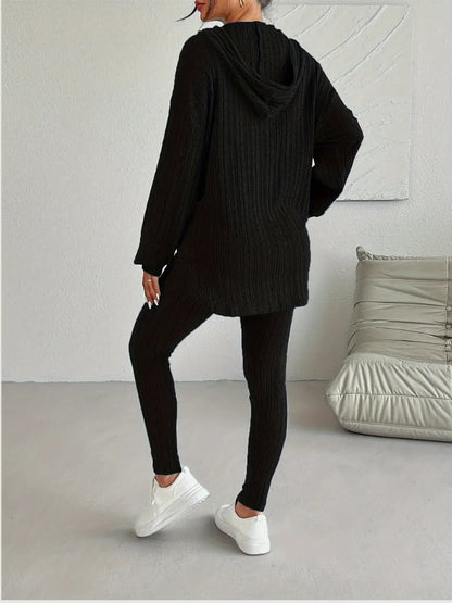 Person wearing a black knit hoodie and leggings in a minimalistic room.
