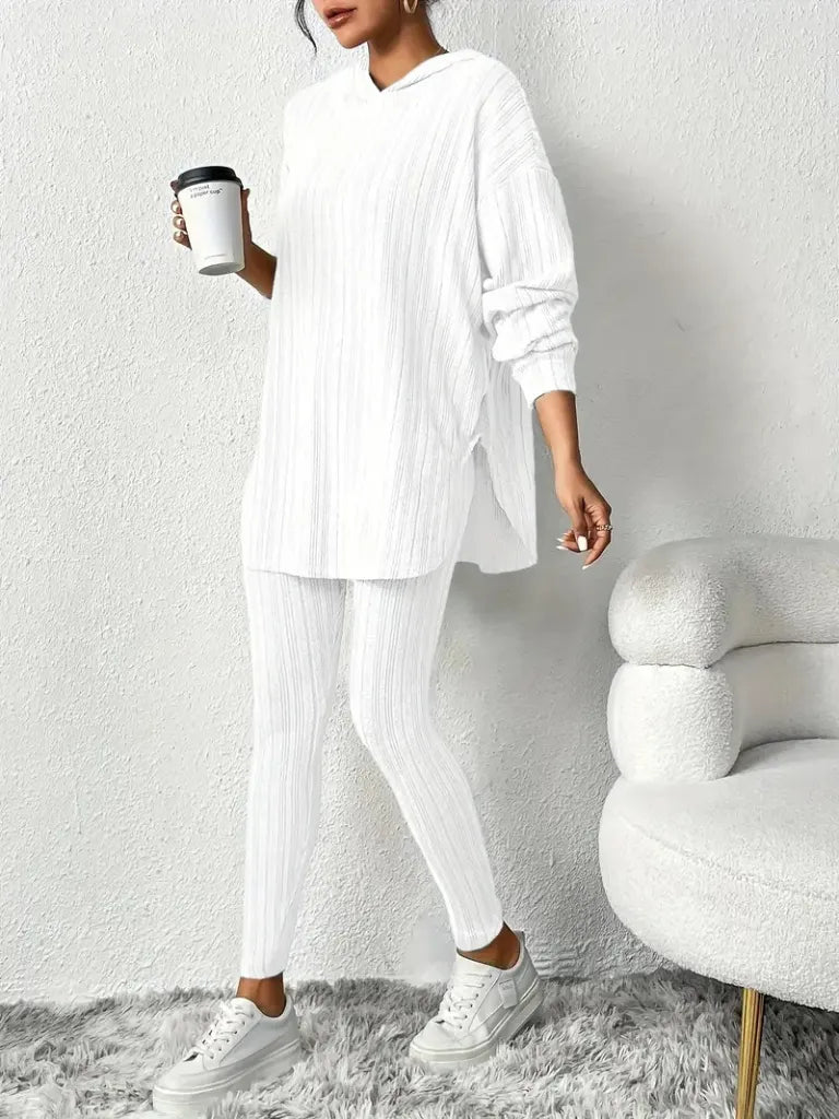 Person wearing a white outfit holding a coffee cup in a minimalistic room.