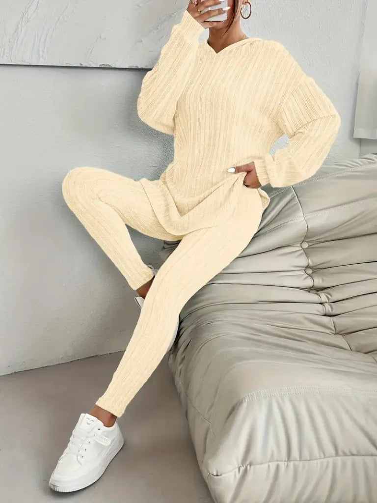 Person wearing a beige knit outfit sitting on a bed.