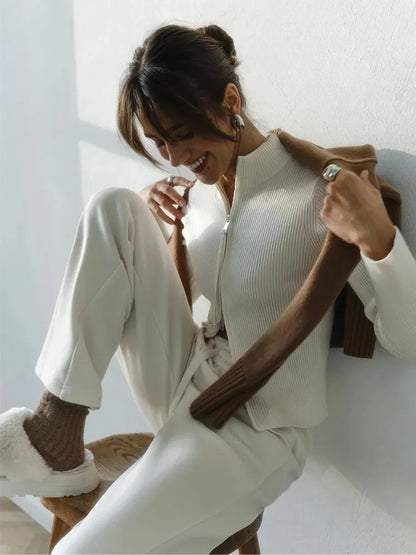 Woman in a white outfit holding a brown jacket against a light background