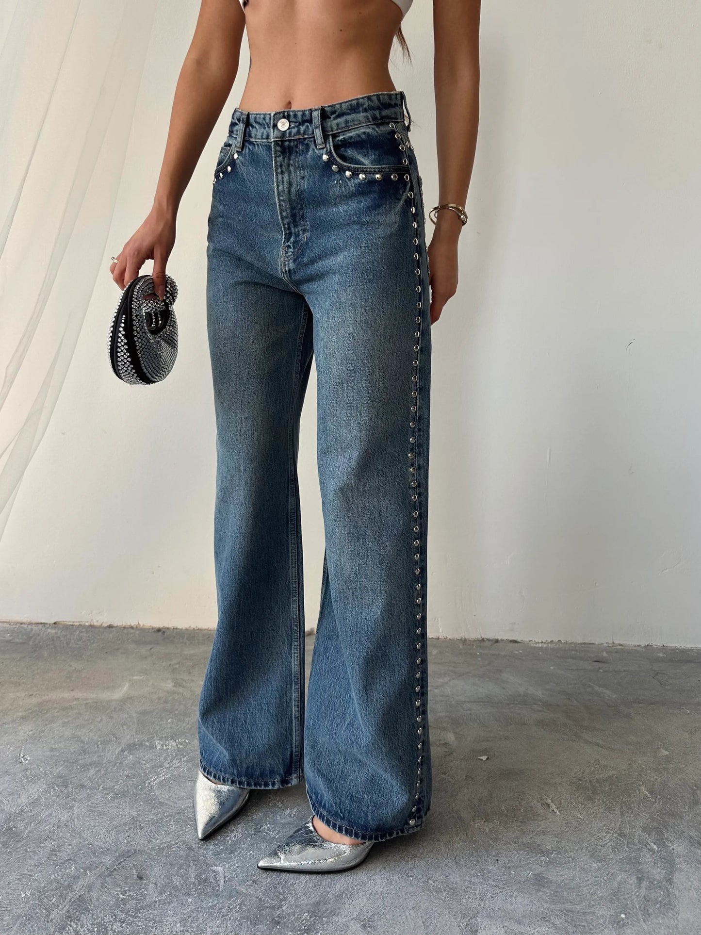 Person wearing high-waisted blue jeans with studded details on a plain background
