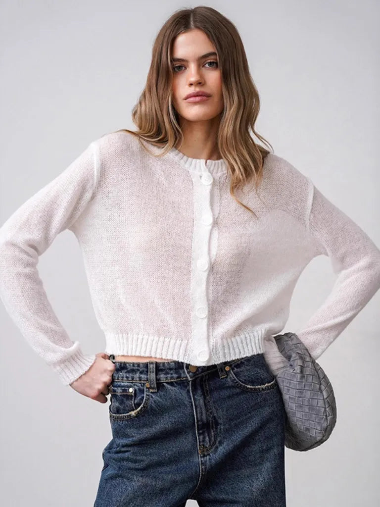Woman wearing a light pink cardigan and blue jeans with a gray bag on a white background