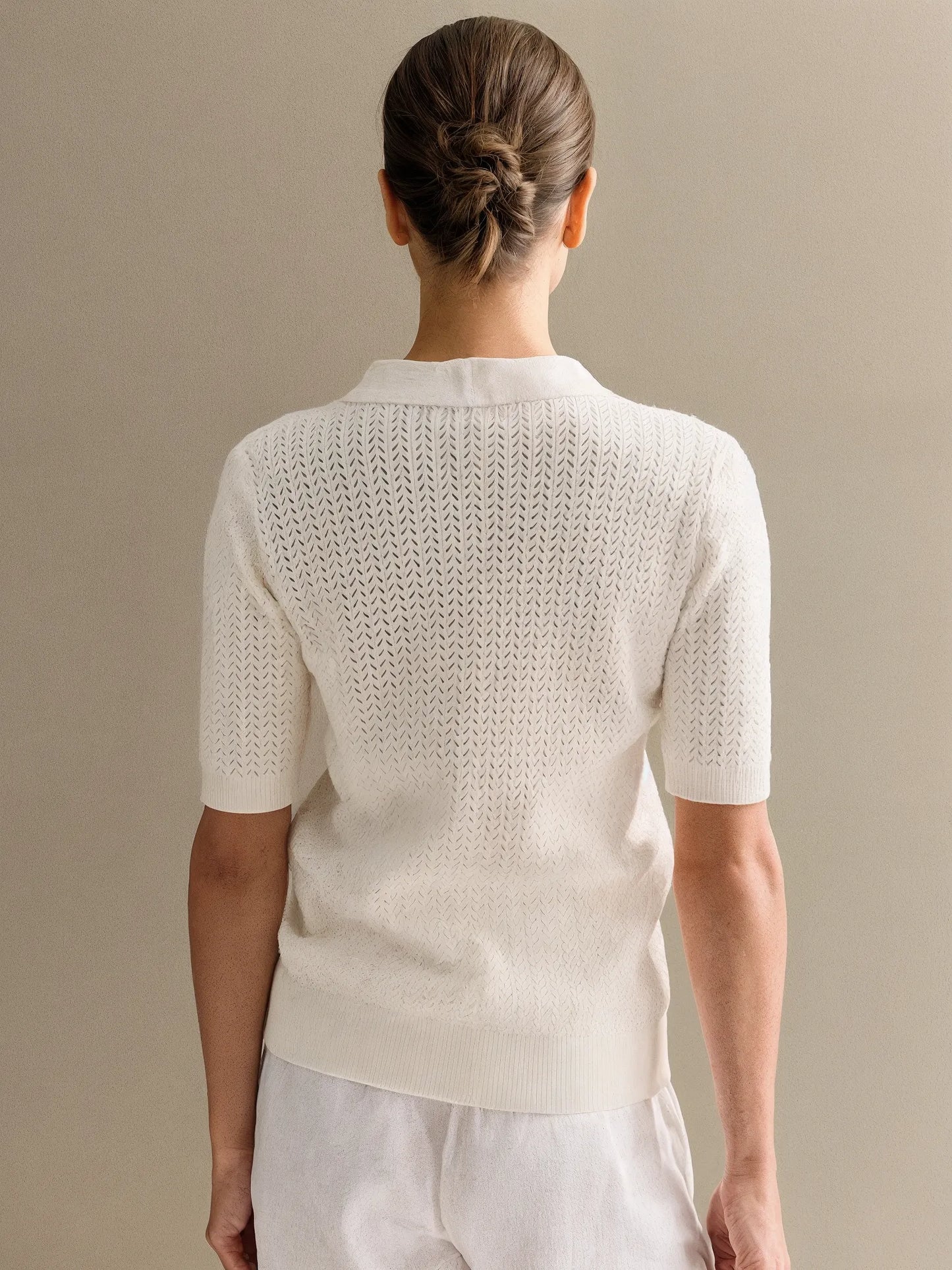 Person wearing a white knit top against a beige background