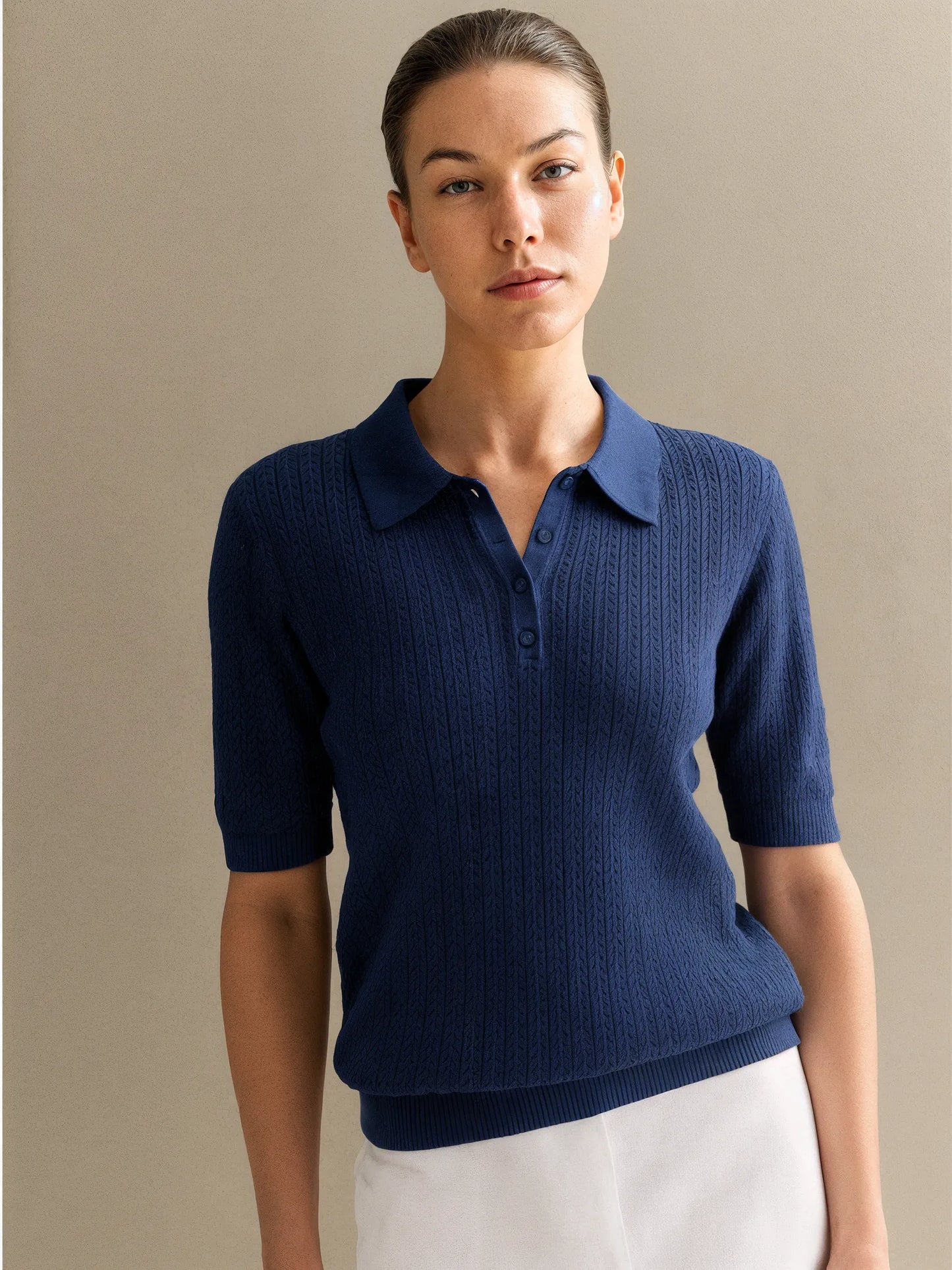 Woman wearing a navy blue knitted polo shirt against a beige background