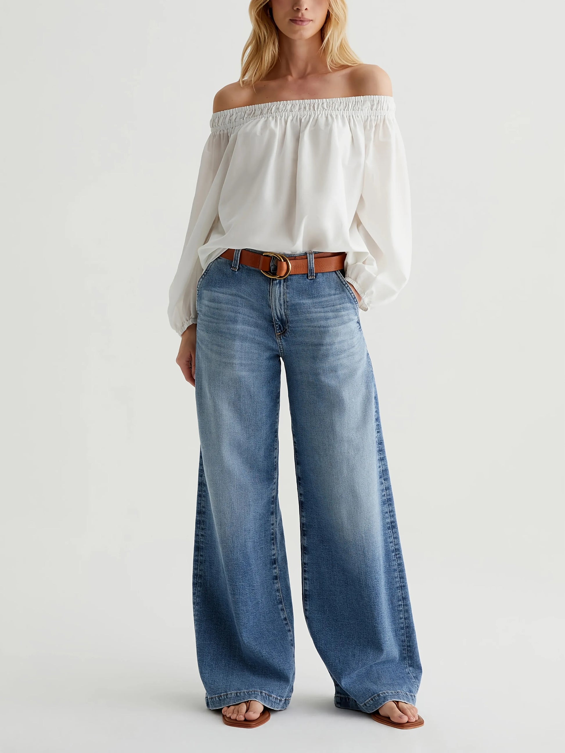 Woman wearing a white off-shoulder top and blue jeans on a white background
