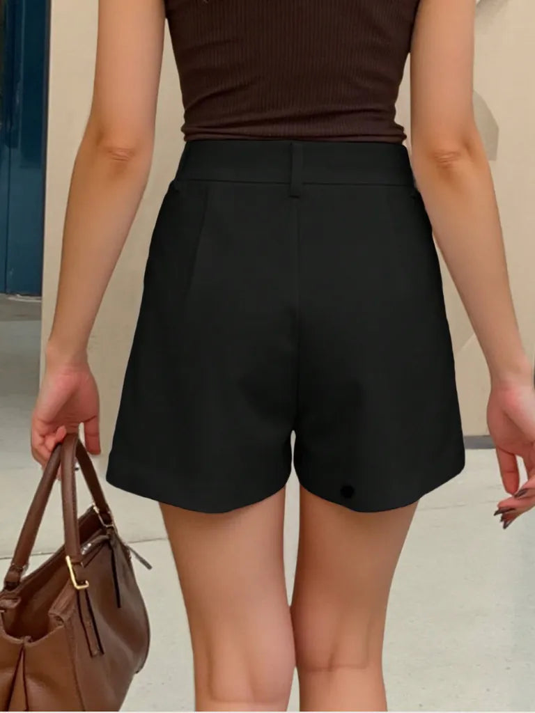 Person wearing black shorts and a brown top, holding a brown handbag.