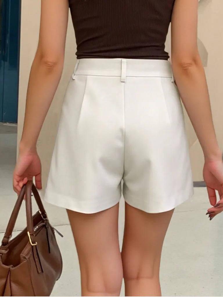 Person wearing white shorts and a brown top, holding a brown handbag.
