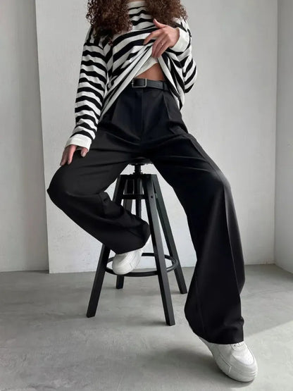 Person wearing a black and white striped sweater and black pants sitting on a stool.