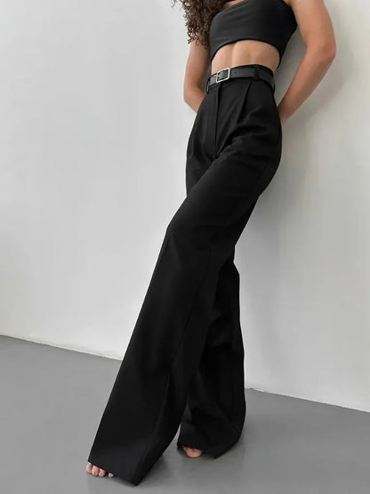 Person wearing a black outfit with wide-leg pants against a white wall.
