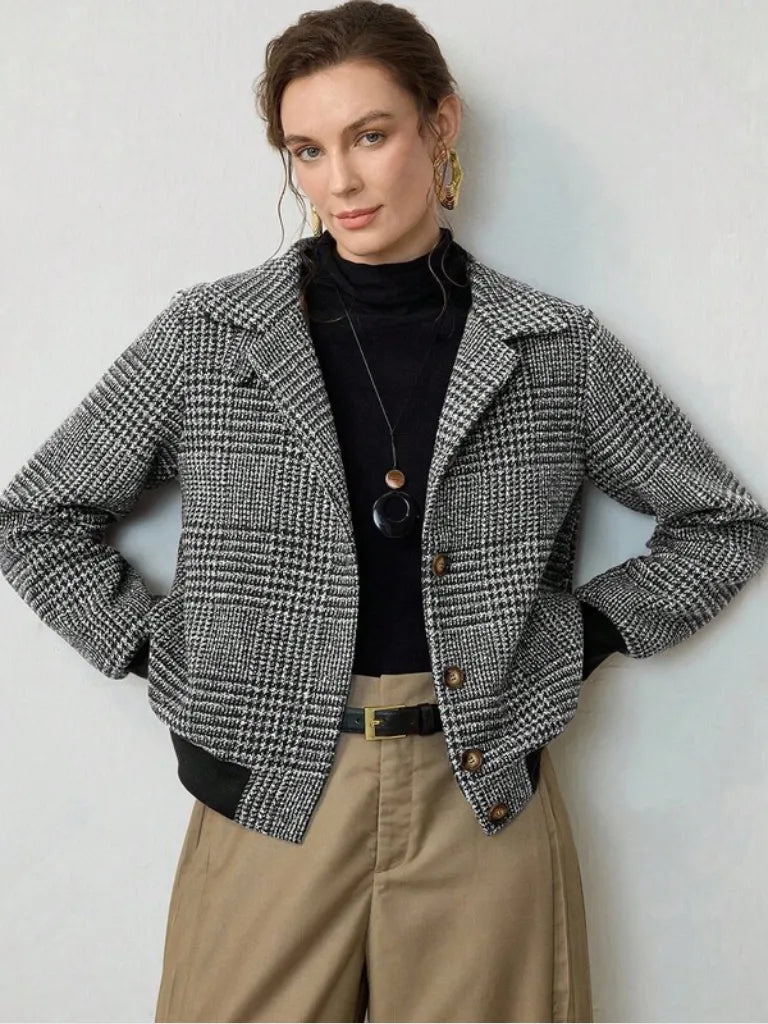 Woman wearing a checkered jacket over a black top and beige pants against a white background