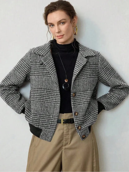 Woman wearing a checkered jacket over a black top and beige pants against a white background