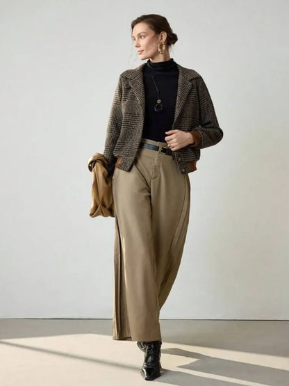 Woman wearing a brown blazer, black turtleneck, and beige pants against a plain background