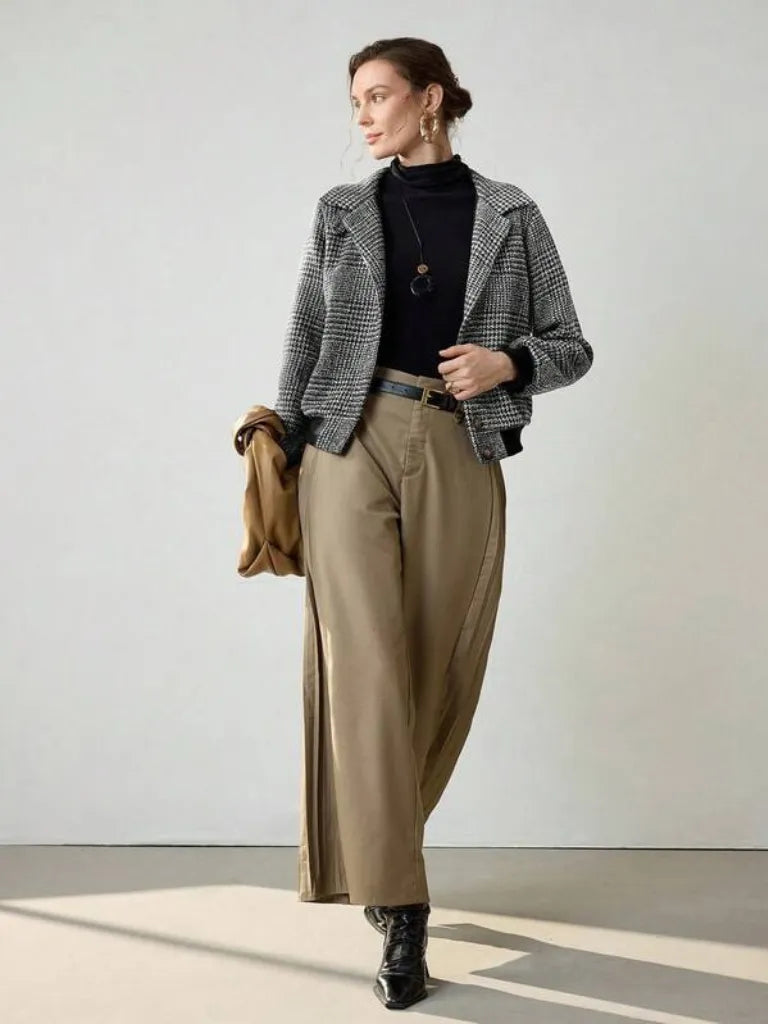 Person wearing a checkered blazer, black turtleneck, beige pants, and black shoes on a light background