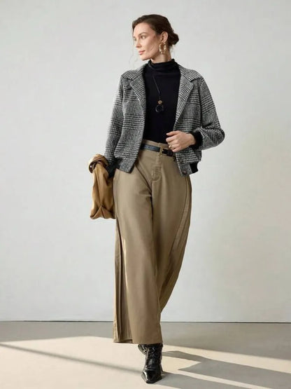 Person wearing a checkered blazer, black turtleneck, beige pants, and black shoes on a light background