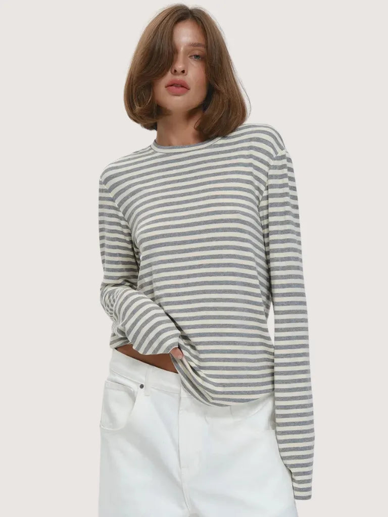 Woman wearing a gray and white striped sweater with white pants on a light background